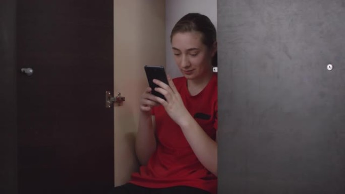 穿着运动服的足球女孩坐在储物柜里，使用智能手机