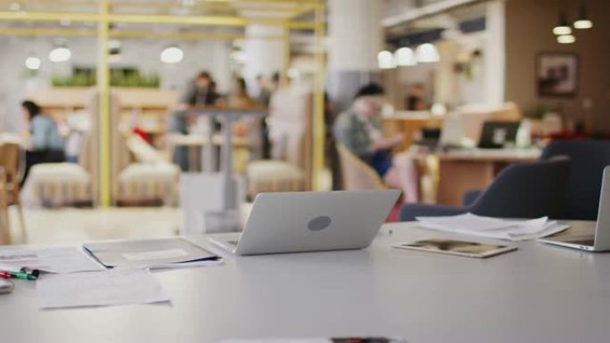 笔记本电脑和繁忙的开放式计划中的办公桌上的文书工作创意办公空间，选择性聚焦
