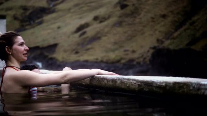 年轻的幸福夫妇在冰岛的温泉游泳。旅行的男人和女人在山里欣赏风景。