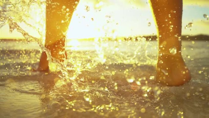 镜头耀斑: 无法辨认的年轻女子在日落时走在玻璃状的海水中。