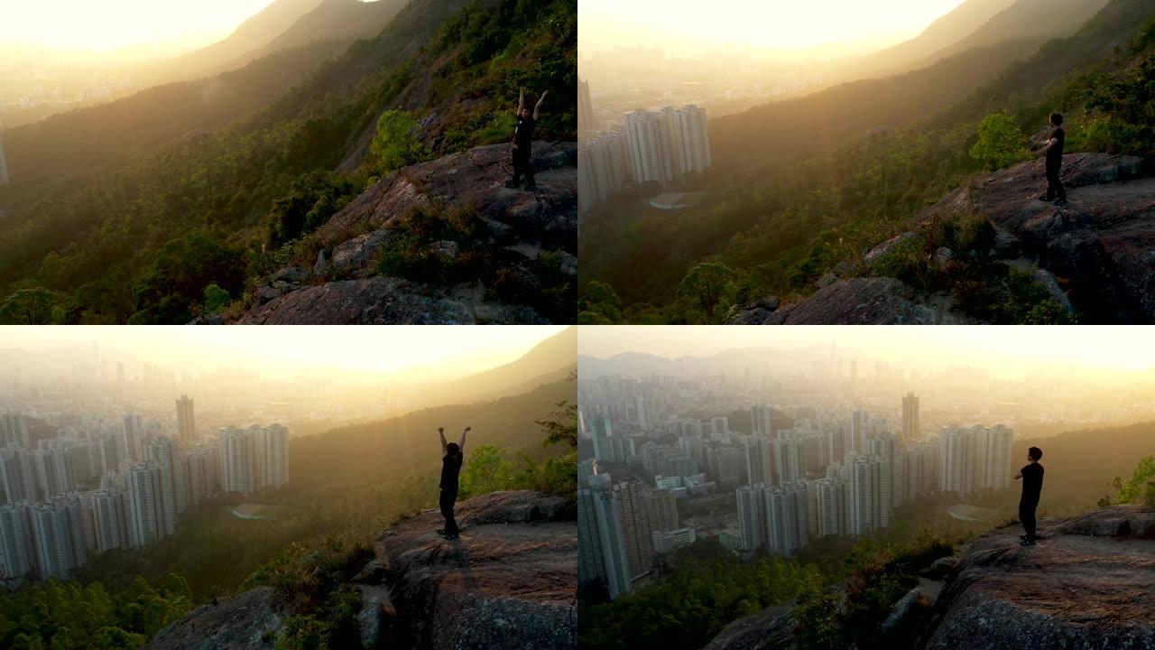 空中飞行的年轻人在美丽的日落中胜利地站在山顶上。成功的姿势伸出武器商业生活成就概念。