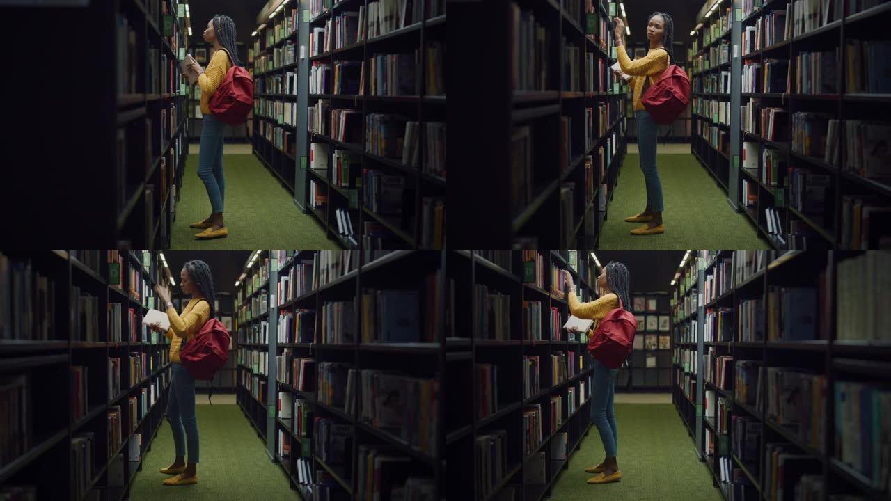 大学图书馆:天才美丽黑人女孩的肖像行走在一排排书架之间寻找合适的书作为课堂作业。专注的聪明学生学习，