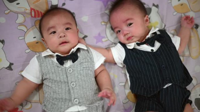 一对5个月大的亚洲华裔双胞胎男婴躺在床上寻求父母的关注