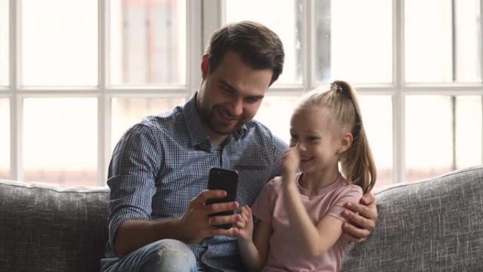 爸爸拥抱小女儿在沙发上玩智能手机