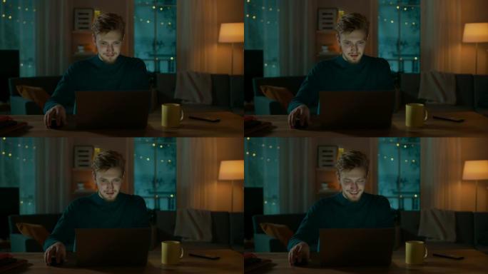晚上在家: 英俊男子坐在办公桌前在笔记本电脑上工作的肖像。微笑的自由职业者在电脑上工作。