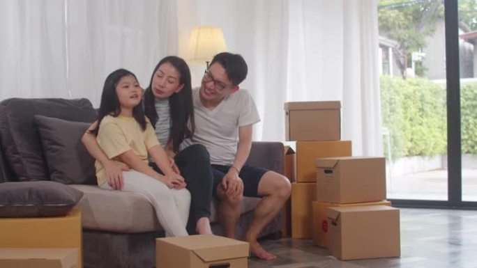 快乐的亚洲年轻家庭房主买了新房。日本的妈妈，爸爸和女儿在搬到沙发上与盒子一起搬家后，对新家的未来充满