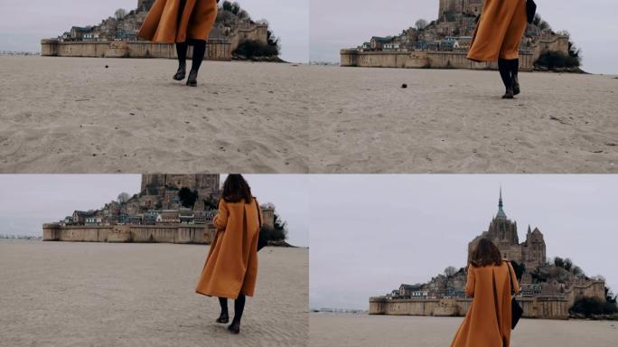 在史诗般的圣米歇尔山慢动作中，时尚的快乐旅行博客写手女人走在柔软的沙滩上。