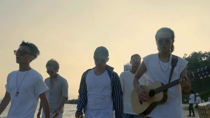 年轻的亚洲成年男子在沙滩上散步唱歌和弹吉他