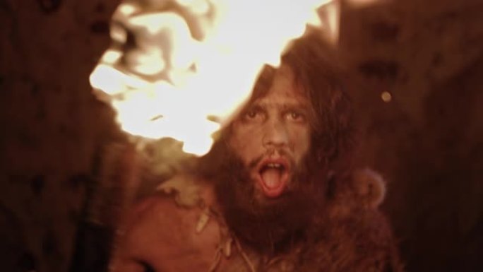 原始穴居人的肖像晚上穿着动物皮站在他的洞穴里，拿着火把攻击。原始尼安德特人猎人/智人尖叫和威胁