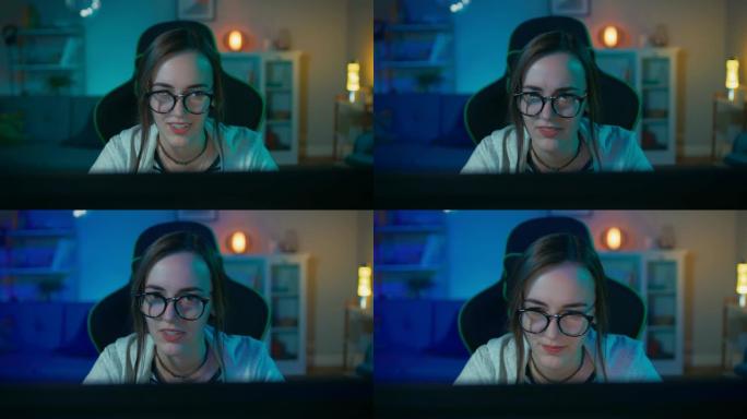 戴着眼镜的兴奋而漂亮的游戏玩家女孩正在她的个人电脑上玩在线视频游戏。房间和电脑有彩色温暖的霓虹灯。在