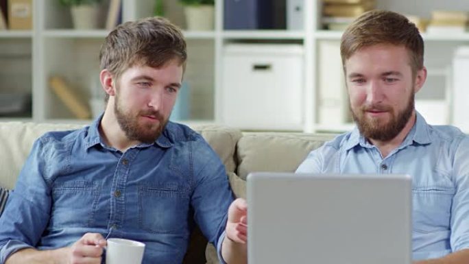 男人使用笔记本电脑并与兄弟交谈