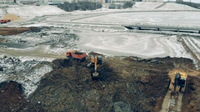 挖掘机和卡车工作的建筑工地上方的鸟瞰图。机器在一个很大的职业生涯中工作。
