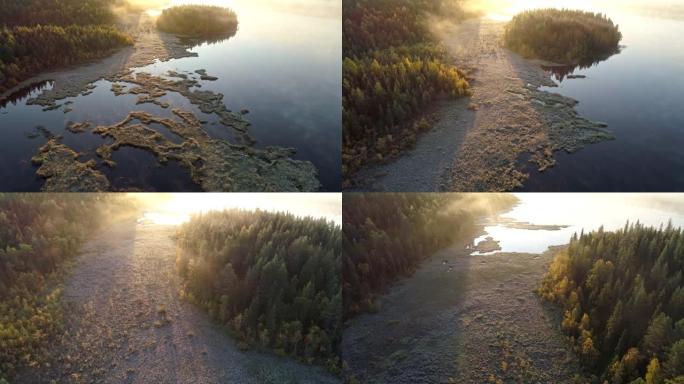 芬兰日出时在雾湖及其海岸上空快速飞行。太阳和阳光反射在湖上。森林覆盖海岸。空中射击，UHD