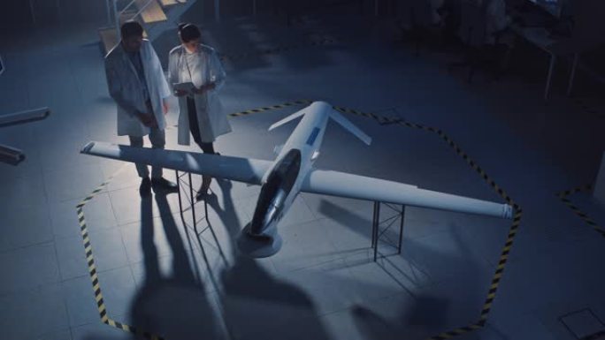 航空航天工程师会议关于无人机/无人机原型的工作。穿着白大褂说话的航空科学家。带有监视或军用飞机的工业