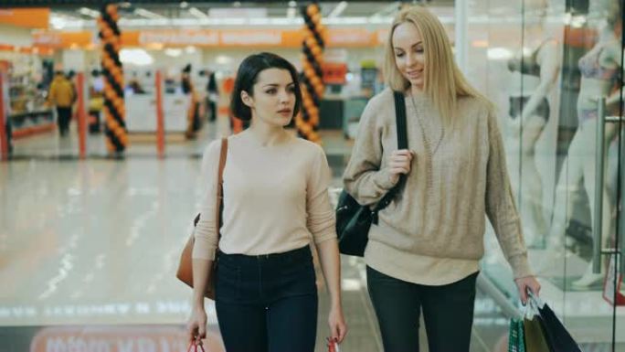 多莉拍摄美丽的女生学生在空闲时间拿着纸袋在购物中心散步时聊天。消费主义、销售和年轻人观念。