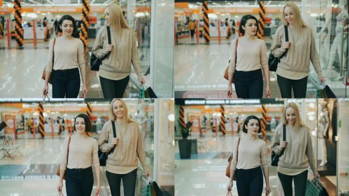 多莉拍摄美丽的女生学生在空闲时间拿着纸袋在购物中心散步时聊天。消费主义、销售和年轻人观念。