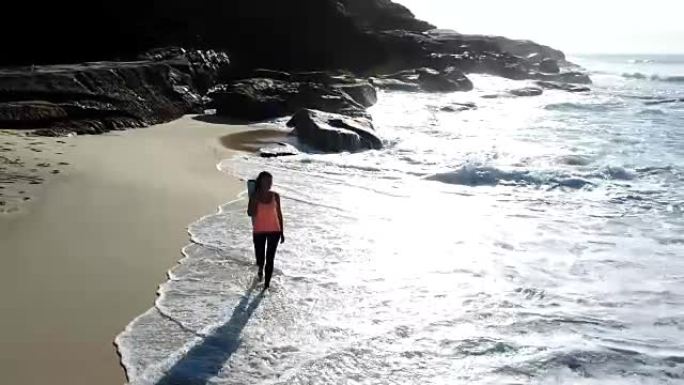美丽的女人带着露齿的微笑，拿着瑜伽垫在沙滩上散步