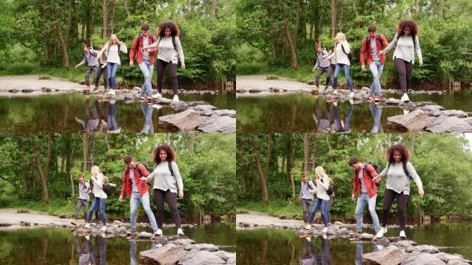 五个年轻的成年朋友在徒步旅行中穿越溪流并站在石头上时手牵手并互相帮助