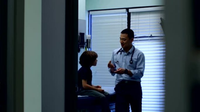 年轻的亚洲男医生在诊所4k向白人男孩患者展示耳朵模型的前视图