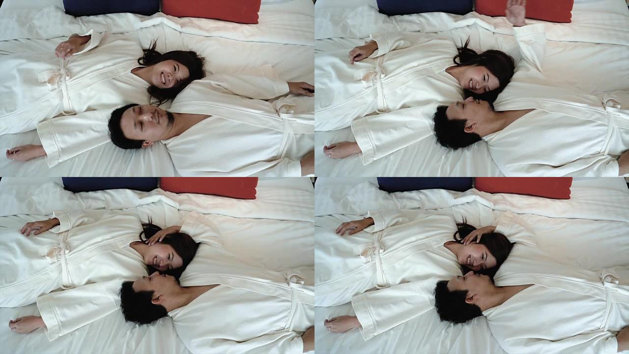 4k慢镜头的亚洲幸福情侣恋爱躺在床上，浪漫的时刻在豪华酒店卧室，生活方式和休闲概念