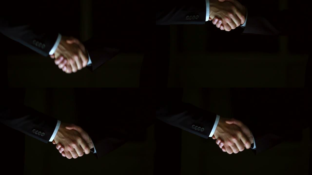 两个男性在黑暗的背景上握手。慢动作