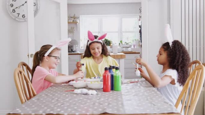 一群女孩坐在厨房桌子旁，戴着兔子耳朵装饰复活节鸡蛋-慢动作拍摄