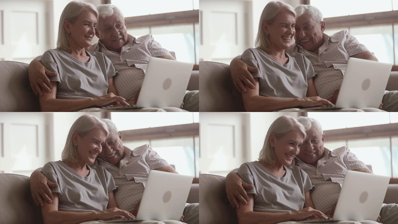 快乐的老年夫妇笑着拥抱一起使用笔记本电脑