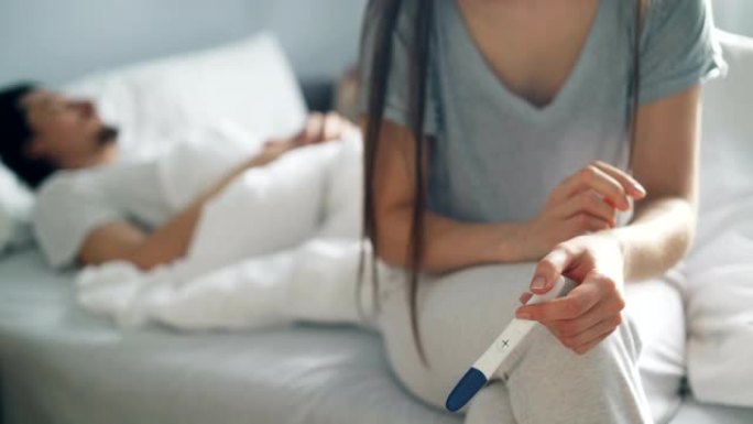 紧张的女人在床上睡觉时保持妊娠试验阳性结果