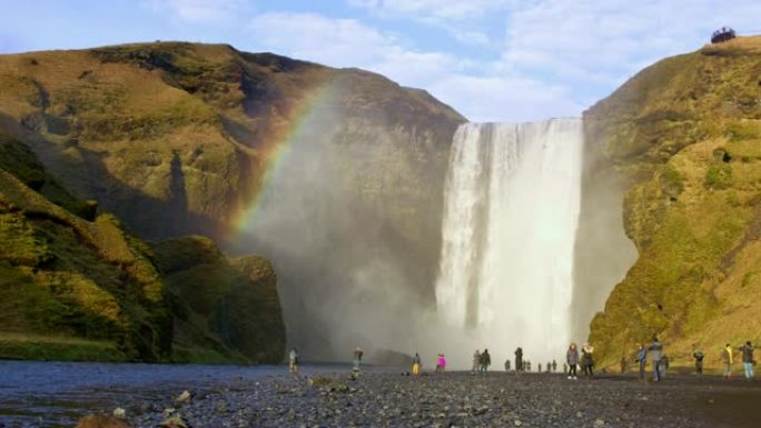 WS游客站在冰岛Skogafoss瀑布阳光明媚的瀑布下