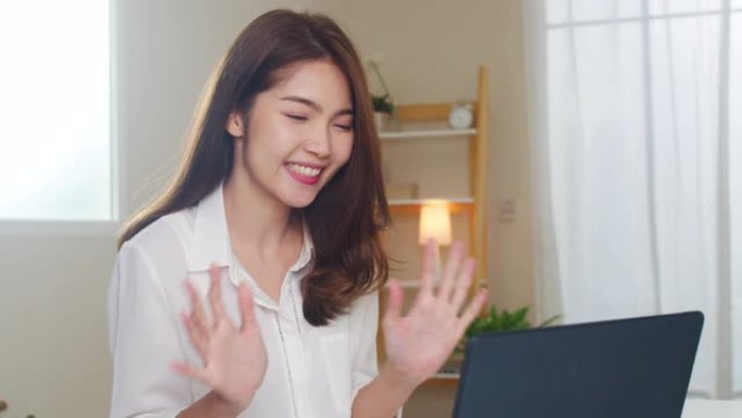 年轻的亚洲商界女性在客厅在家工作时使用笔记本电脑视频通话与情侣交谈。