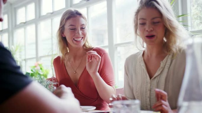 两名年轻的成年白人妇女在低角度餐厅与朋友共进午餐