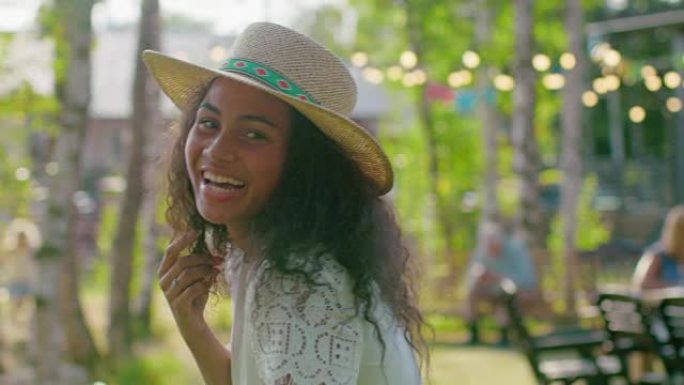 戴着帽子的美丽黑人女孩的肖像迷人地微笑着，抚摸着她的头发。夏日迷人的女孩在花园里放松。慢动作。