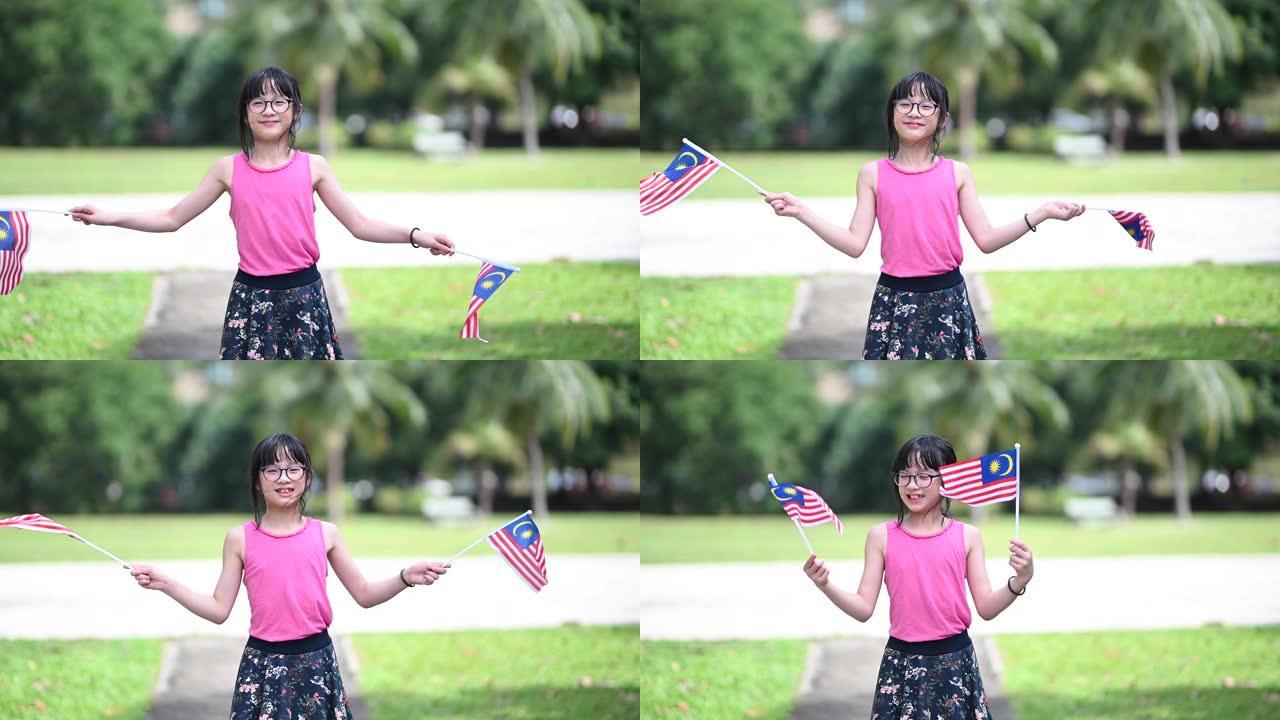 一位亚洲华裔女孩在公园里挥舞着马来西亚国旗，看着镜头