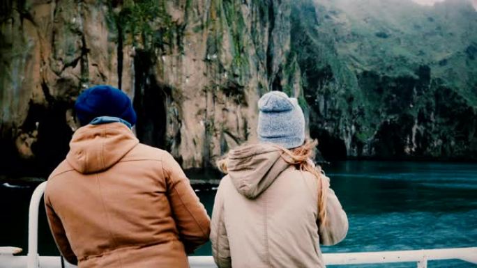 年轻的时尚夫妇站在船上，看着冰岛路过的岛屿。