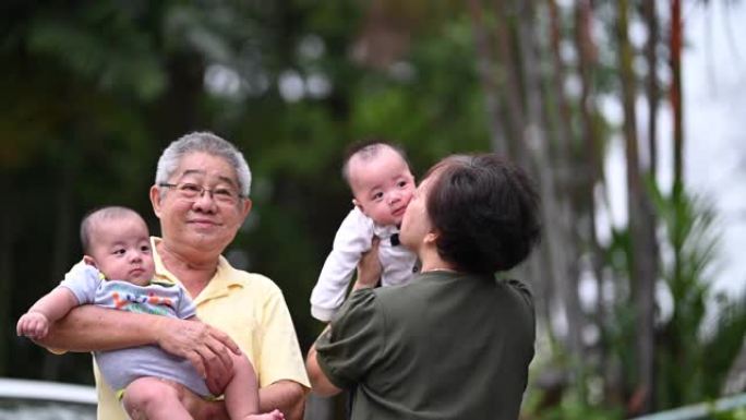 一对亚洲华裔高级夫妇在他们家前院与孙子玩耍