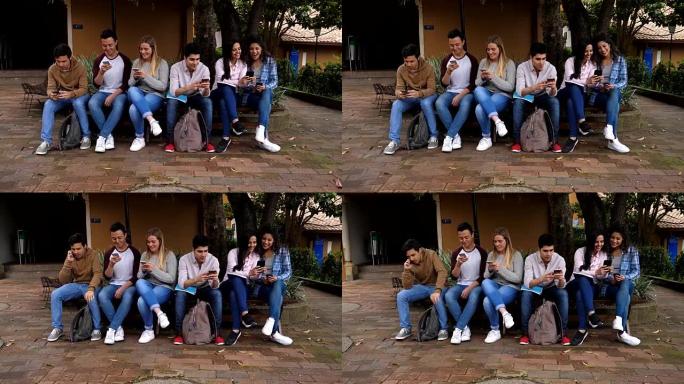 一群大学生坐在外面的校园里用手机聊天