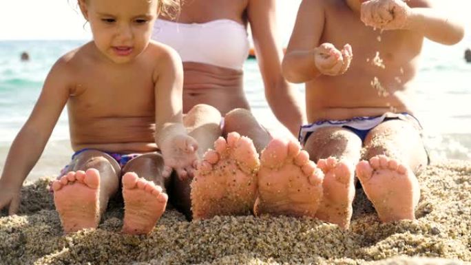 一家人在海边的沙滩上玩耍，双腿和手指都很小，穿着泳衣，背景是黄沙和碧水。
