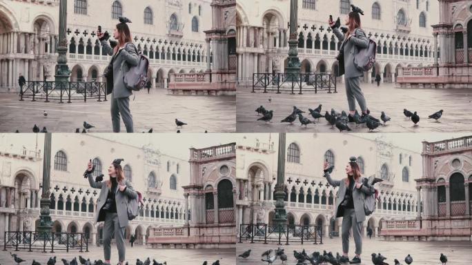 快乐微笑的女游客，鸽子坐在她的胳膊和头上，在威尼斯慢动作的城市广场上自拍。