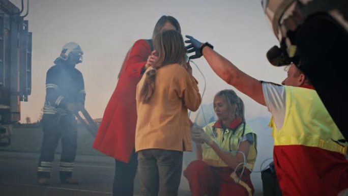 车祸: 受伤的年轻女孩与她慈爱的母亲团聚，护理人员给氧气面罩。在背景中翻车和勇敢的消防员拯救生命