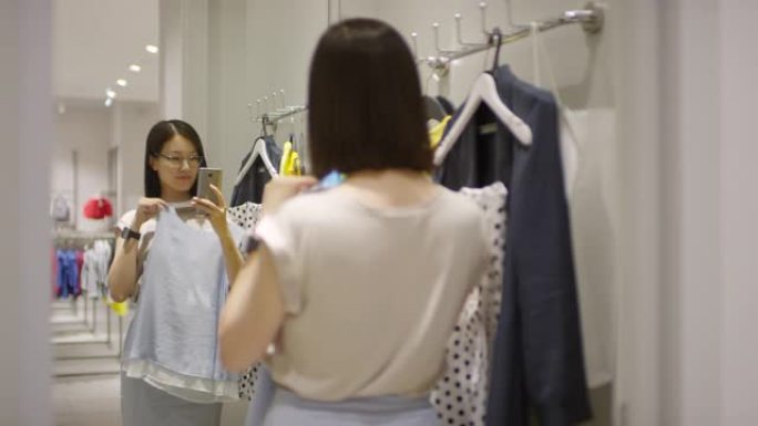 亚洲妇女在试衣间镜子里用衬衫自拍
