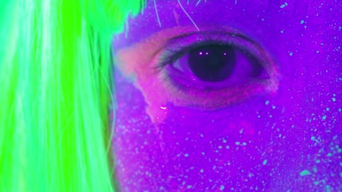 特写女性眼睛与荧光化妆绿色，假发，创意化妆看起来非常适合夜总会。万圣节派对，表演和音乐概念-慢动作视