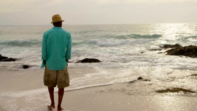 非裔美国人男子双手插在口袋里在海滩上行走的后视图4k