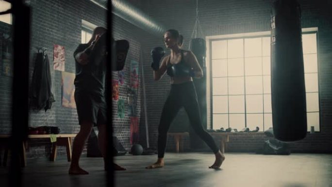 健身运动女性跆拳道运动员在健身房锻炼时拳击垫。她美丽而充满活力。强壮的教练拿着拳击垫。激烈的自卫训练