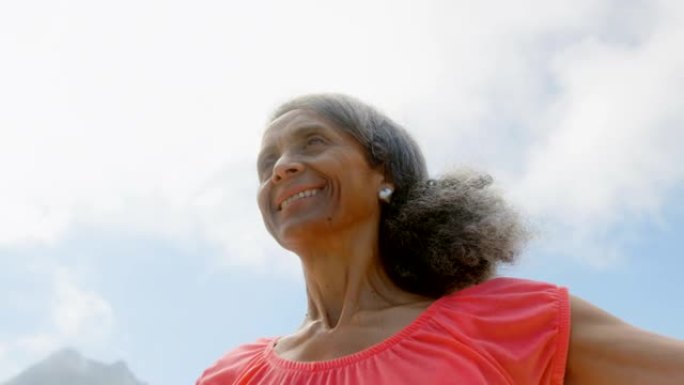 活跃的非裔美国高级妇女在沙滩上的阳光下伸展手臂的低角度视图