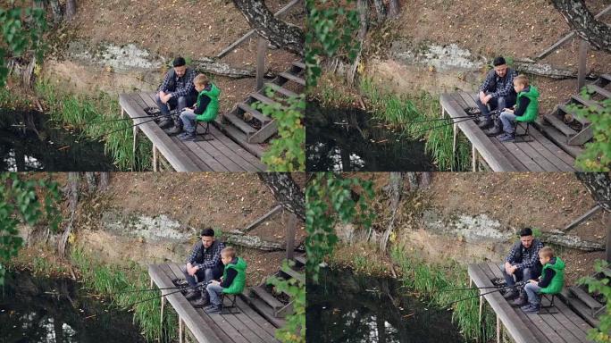 秋天的时候，小男孩和他的爸爸从木制码头在湖里钓鱼，孩子拿着棍子坐在椅子上，而他的父亲正在和他说话。自