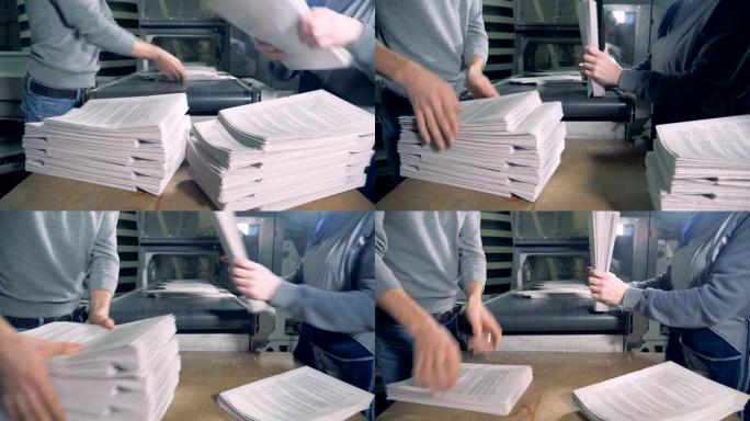 人们从印刷输送机上取出成堆的纸。