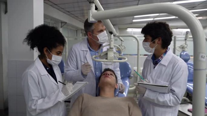 老师检查病人的牙齿，旁边的学生问问题