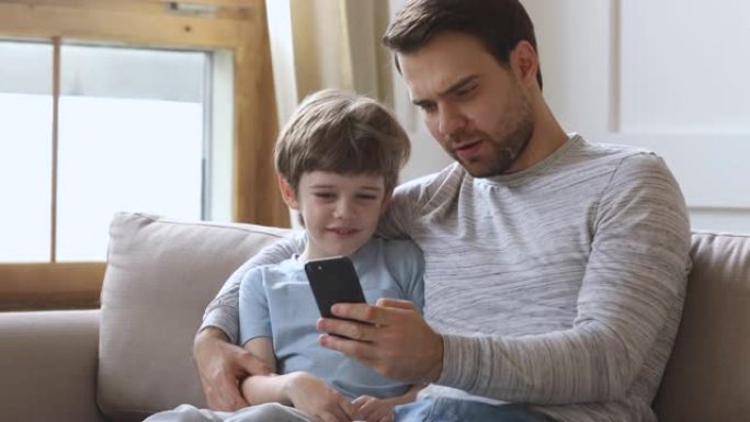爸爸教孩子儿子在沙发上用手机玩得开心