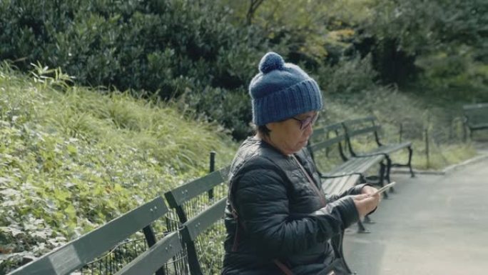 亚洲老年人用智能手机拍照并坐在公园长椅上