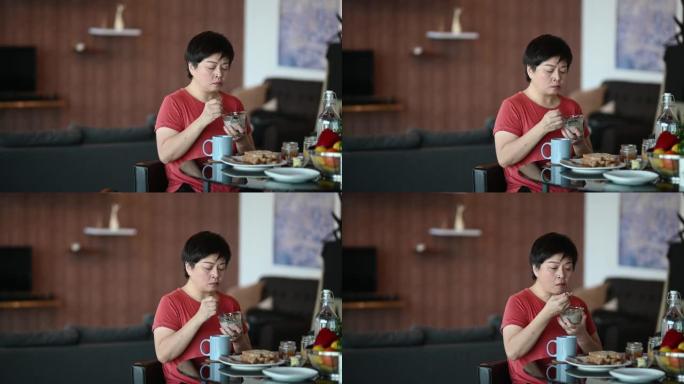 一位成年妇女早上在她的公寓里享用早餐，看着微笑着吃麦片